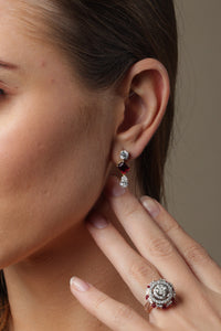 Woman wearing jewelry, including earrings and a ring, against a neutral background