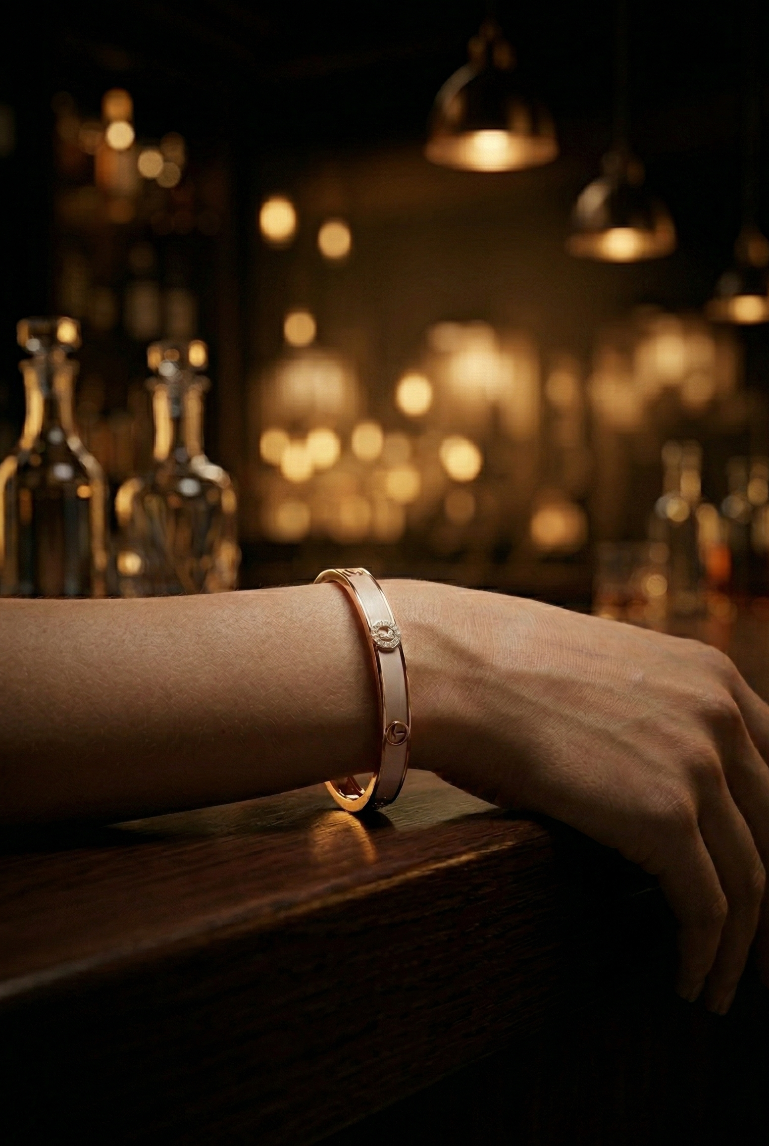 Hand wearing a bracelet on a bar counter with blurred bottles in the background