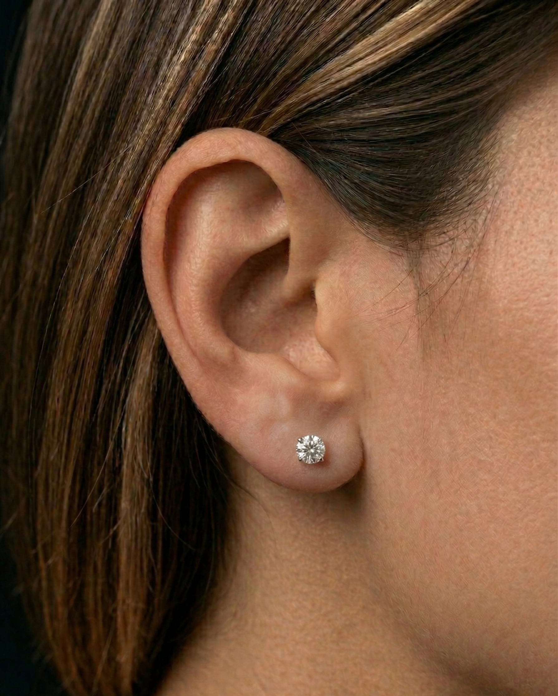 Close-up of an ear wearing a diamond stud earring with blurred background