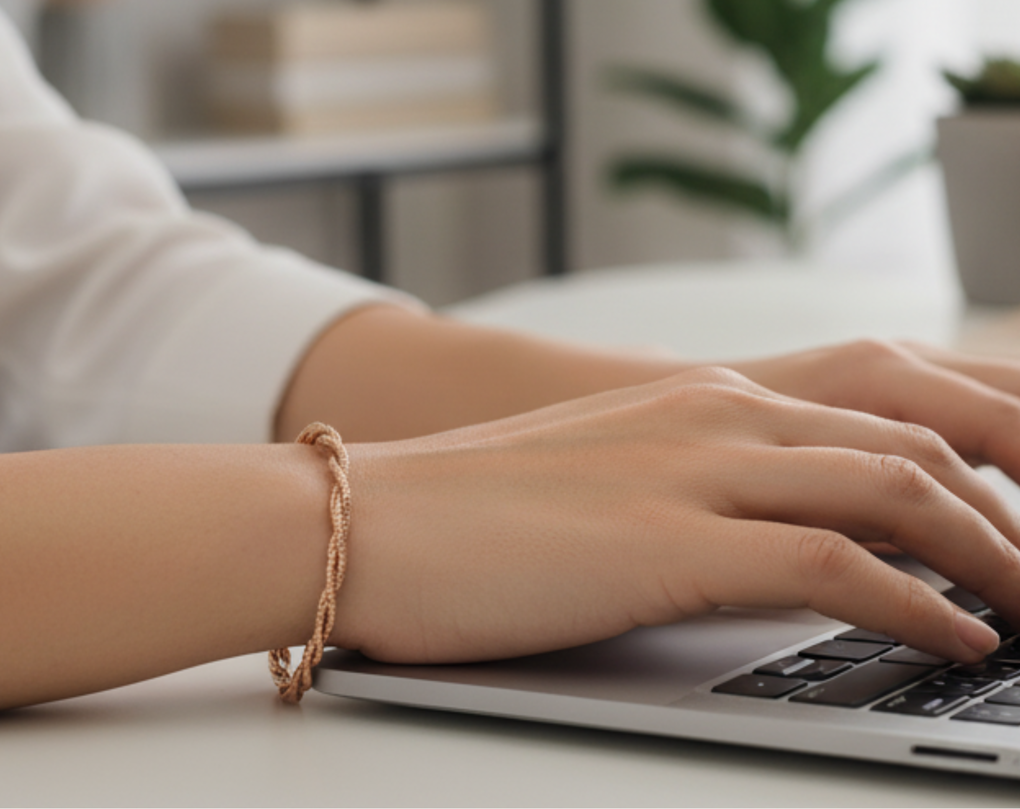 Person typing on a laptop with a blurred background of a home office.